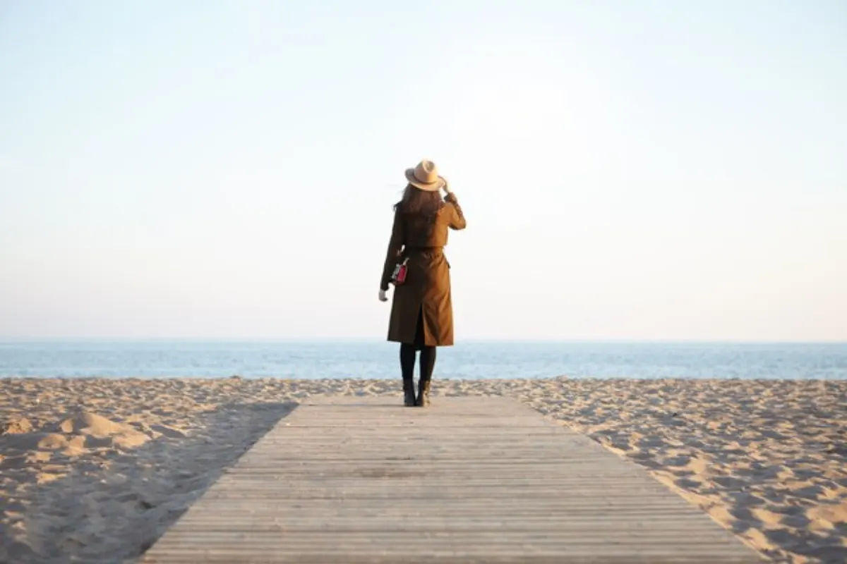 A woman walking along a boardwalk toward the ocean, symbolising clarity and forward direction