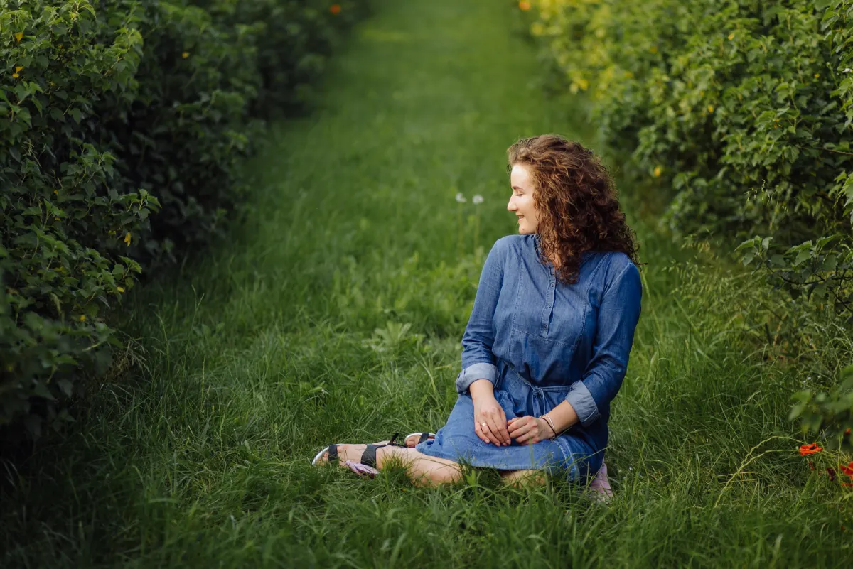 A woman sitting peacefully in nature, grounded and comfortable in herself